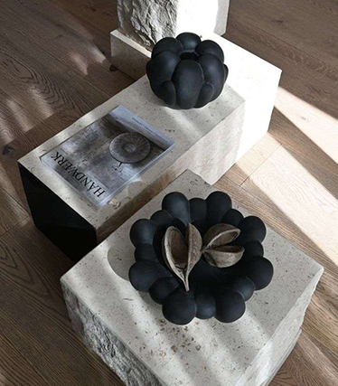 Umělecké černé keramické mísy na minimalistických kamenných stolech s přírodní strukturou.