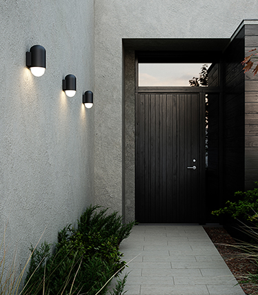 Moderní venkovní nástěnná světla osvětlují vstup do moderního domu při soumraku.