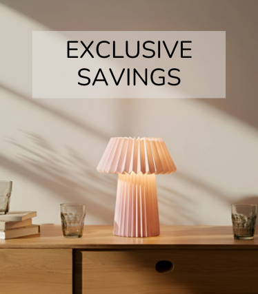 Halvány rózsaszín asztali világítás egy fából készült komódon, körülötte poharak és könyvek a meleg napfényben.